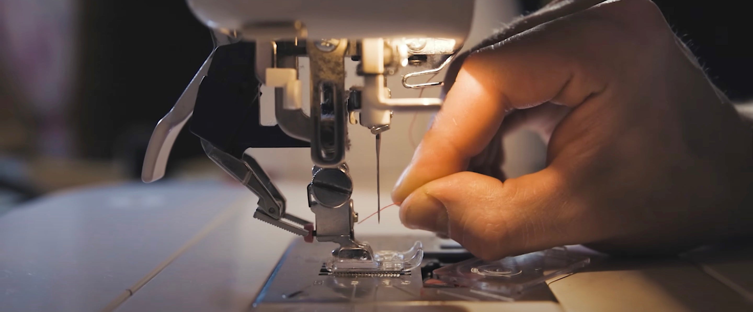 Close-up of a sewing machine needle and thread with a hand guiding fabric.