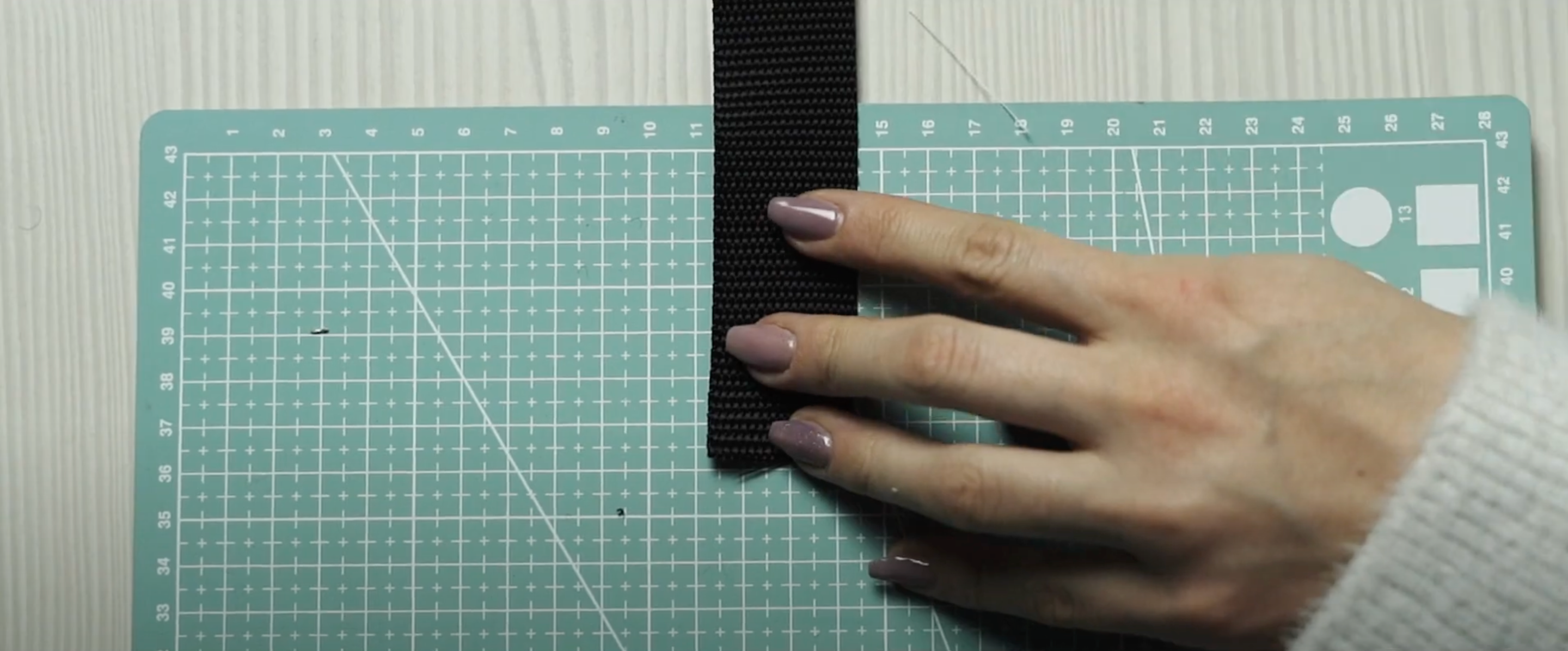 Hand holding a black strip of material on a green cutting mat with grid lines.