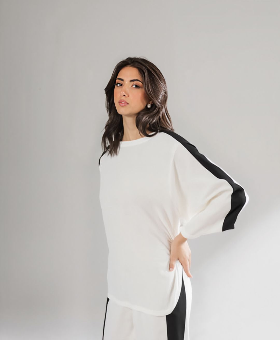 Woman wearing a white sweater with black sleeves against a plain background